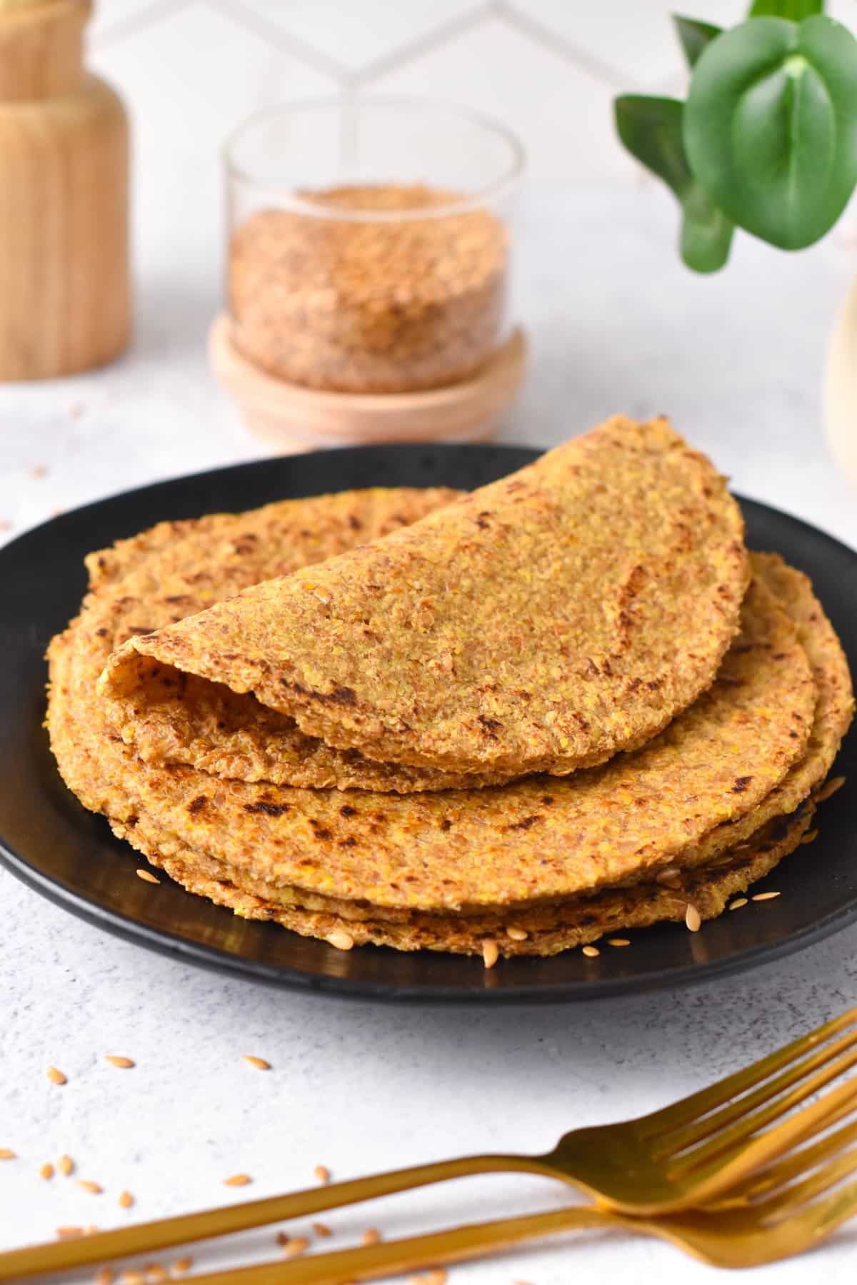 Flaxseed tortillas made with ground flaxseeds and water on a black plate with a jar full of flaxseeds in the background.