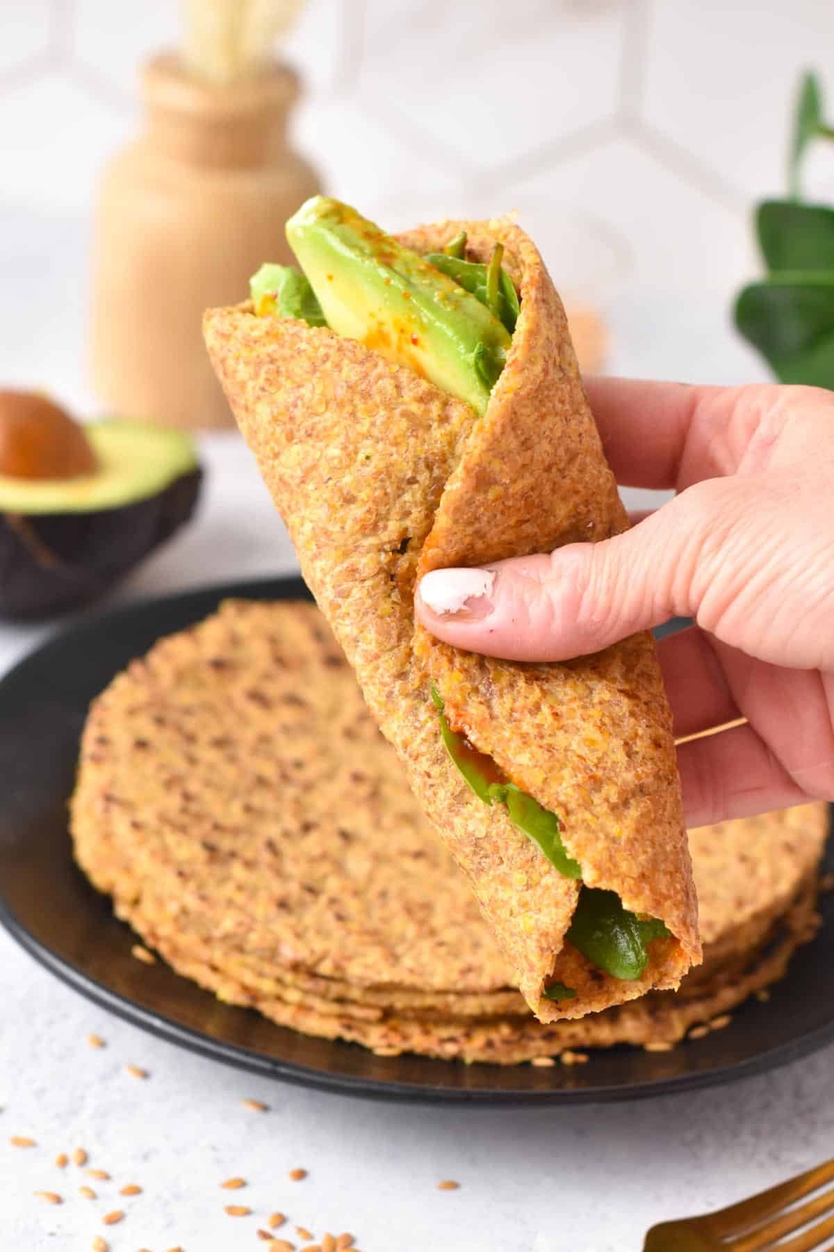 Holding rolled flaxseed wraps filled with avocado and baby spinach.