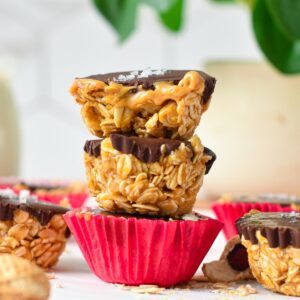 a stack of three no-bake peanut butter oat cups with the one on top half cut showing the runny peanut butter filling