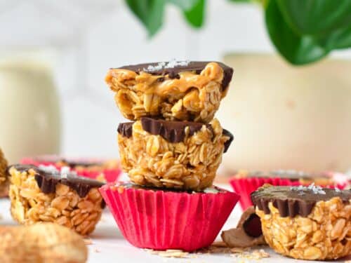 a stack of three no-bake peanut butter oat cups with the one on top half cut showing the runny peanut butter filling