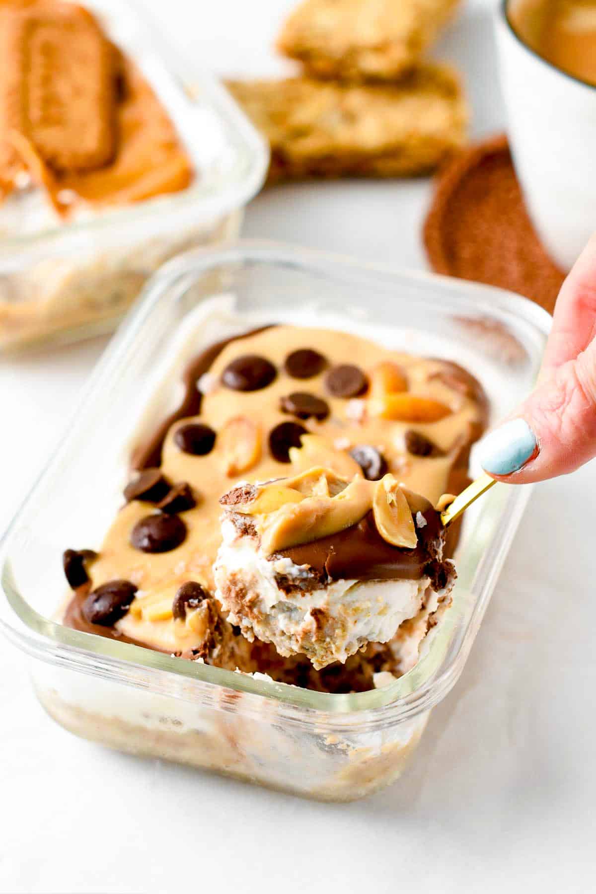 A spoon taking a serving out of a rectangle glass container filled with Nutella Overnight Weetbix and topped with peanut butter, chocolate chips and peanuts