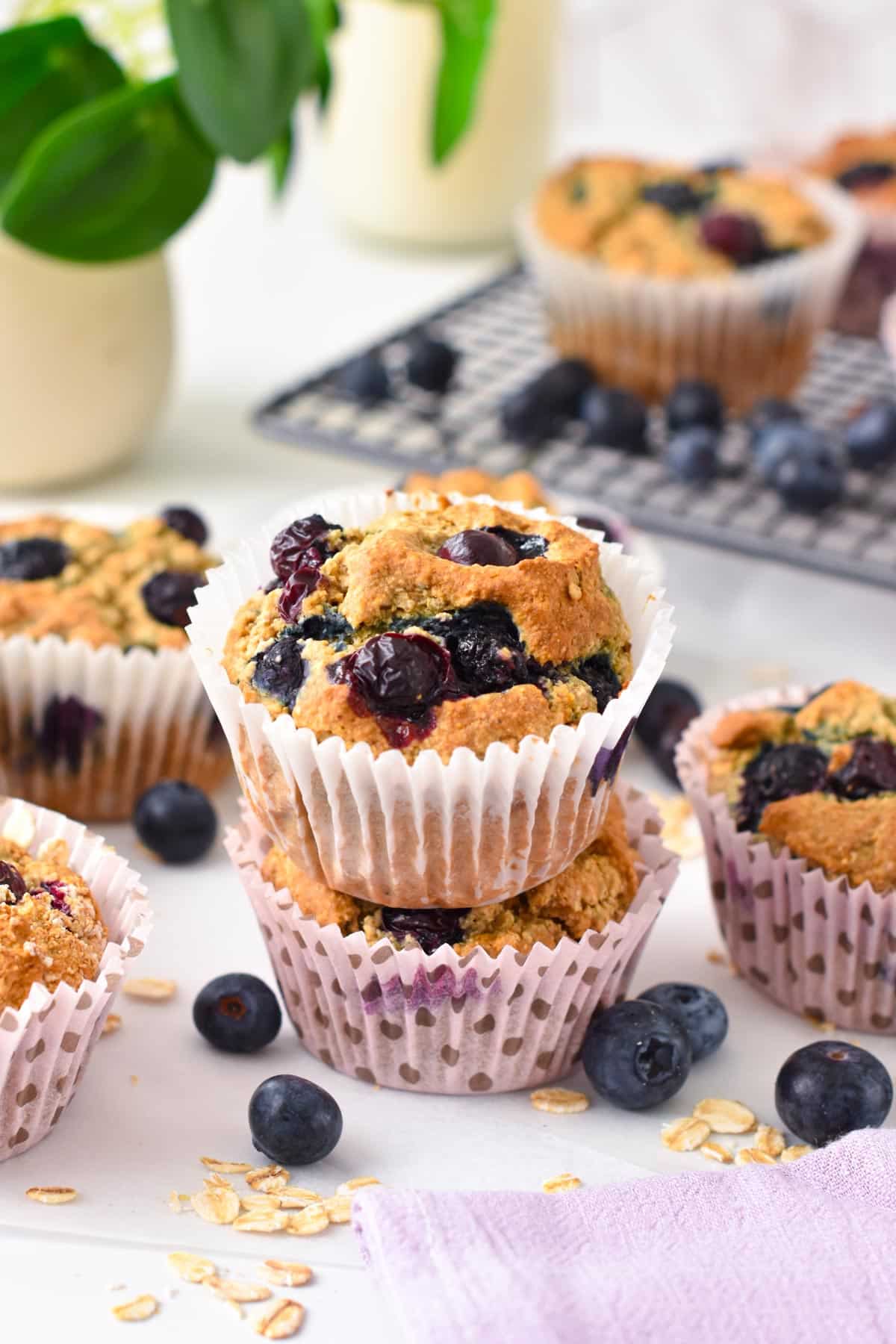 A stack of two Vegan Gluten Free Blueberry Muffins next to more muffins and fresh blueberries,