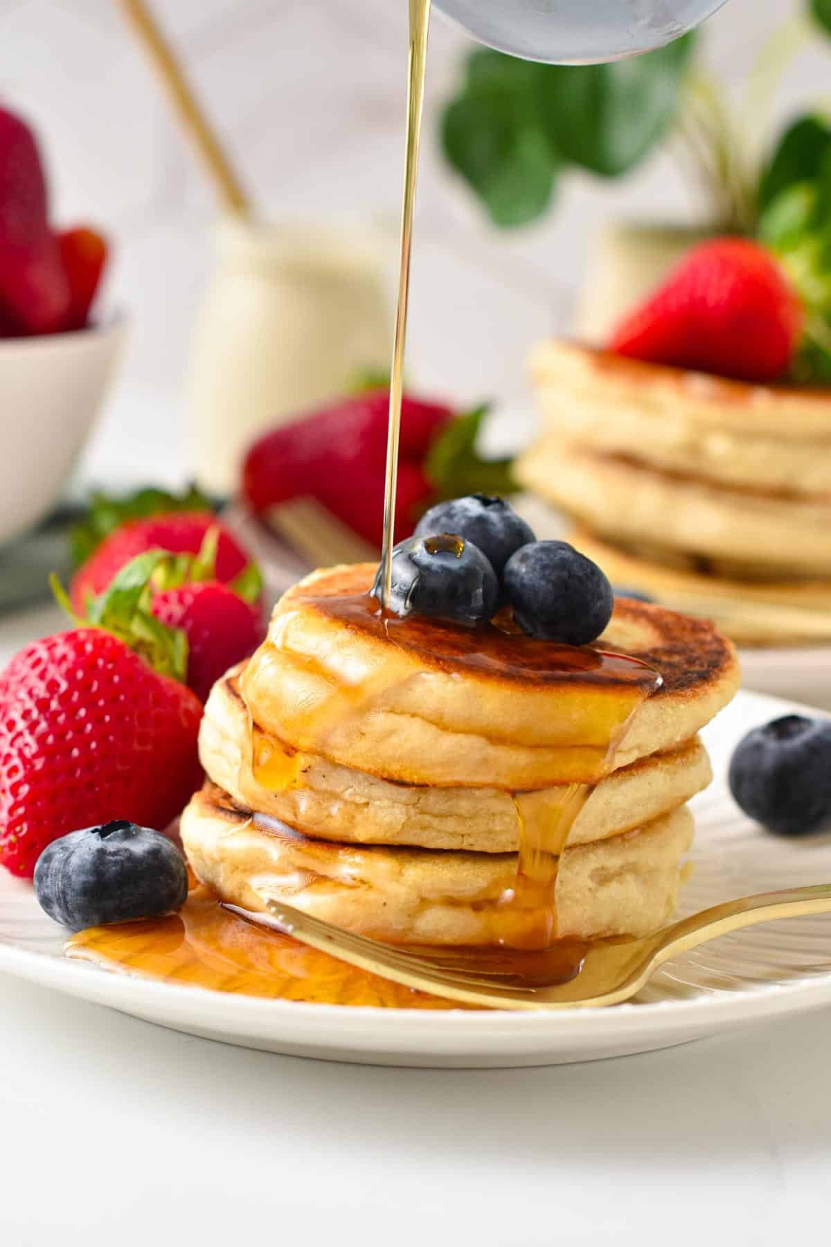 A stack of vegan pancakes topped with blueberries and a drizzle of maple syrup.