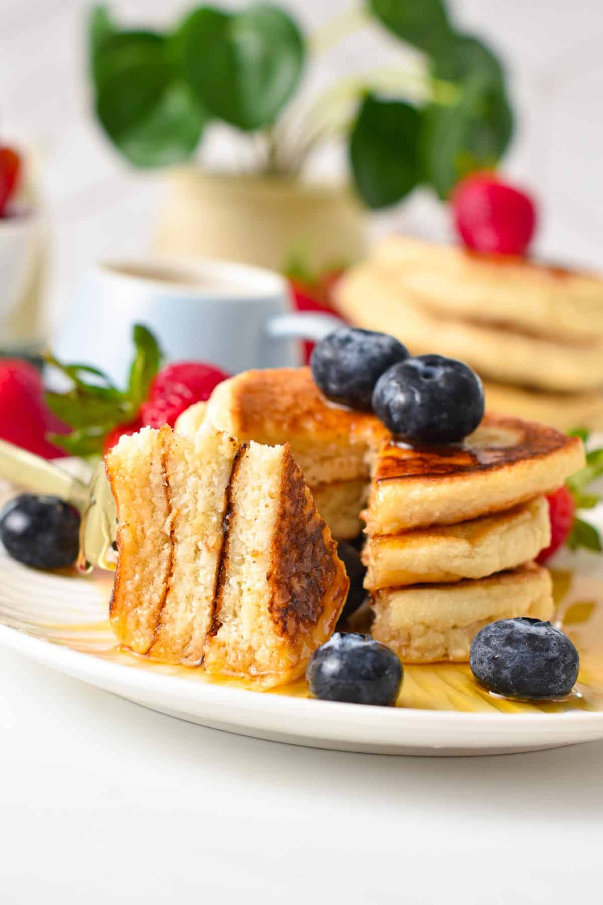 A stack of Vegan Coconut Flour Pancakes sliced in the middle and showing the fluffy pancake texture inside.
