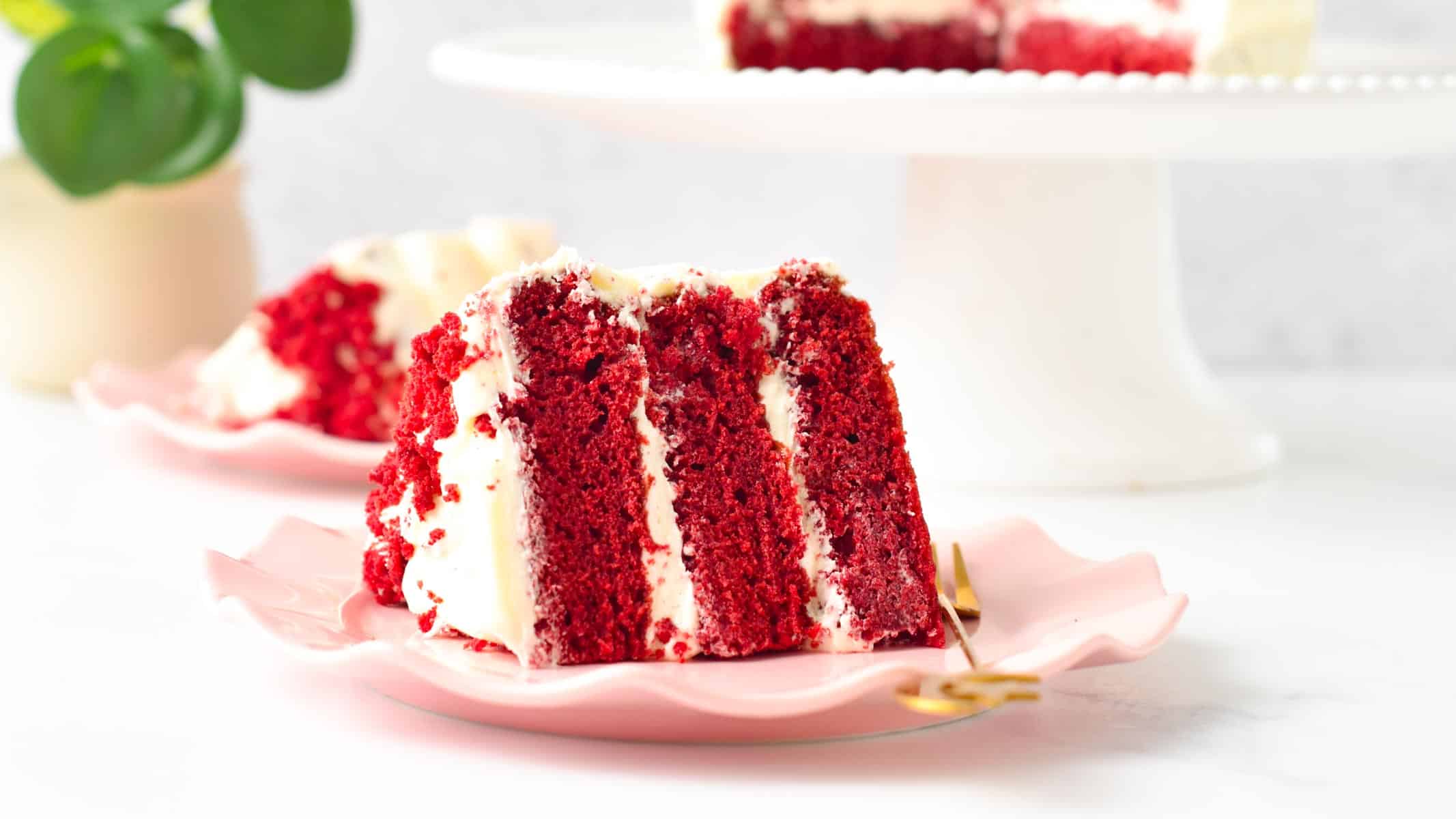 a slice of vegan red velvet cake with three layers and filled with dairy-free cream cheese frosting