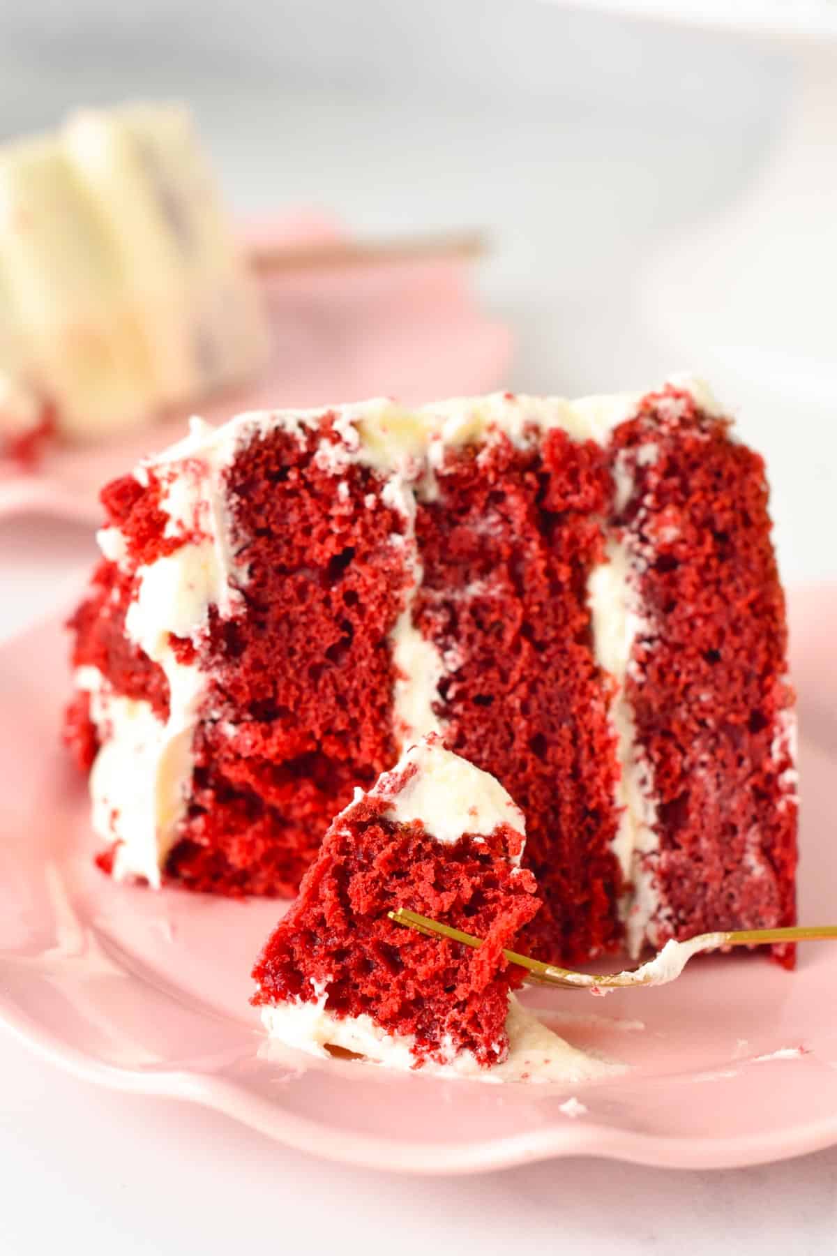 A close-up view of a slice of vegan red velvet cake with three layers and filled with dairy-free cream cheese frosting