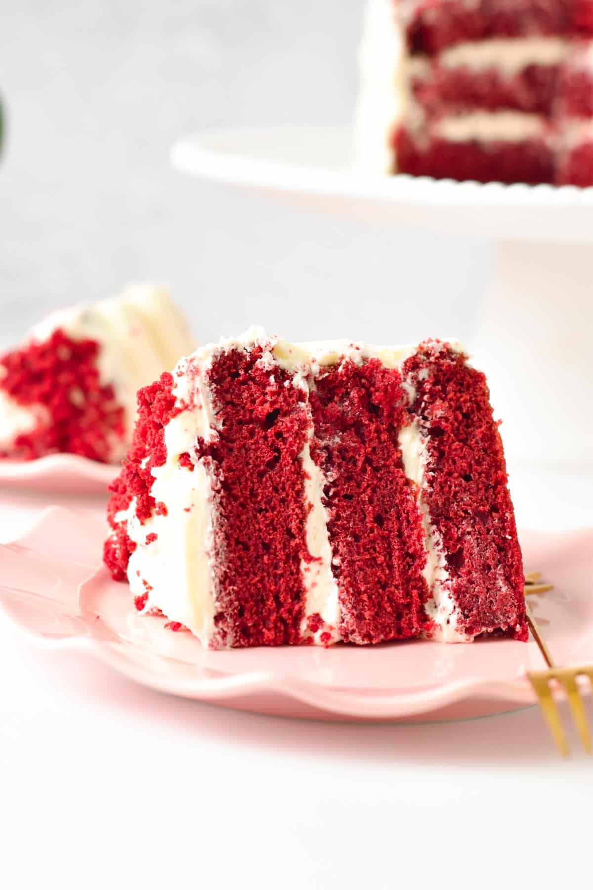A slice of vegan red velvet cake with three layers and filled with dairy-free cream cheese frosting.