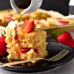 A plate filled with a stack of two vegan sheet pan pancakes, fresh strawberries, dairy-free whipped cream and a drizzle of maple syrup