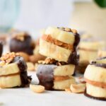 a stack of banana bites filled with peanut butter in the center and half covered with dark chocolate