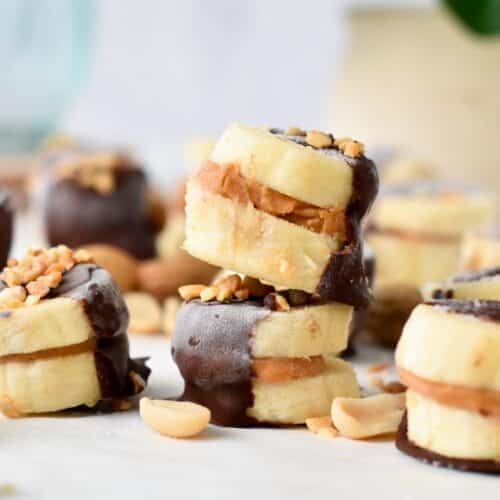 a stack of banana bites filled with peanut butter in the center and half covered with dark chocolate