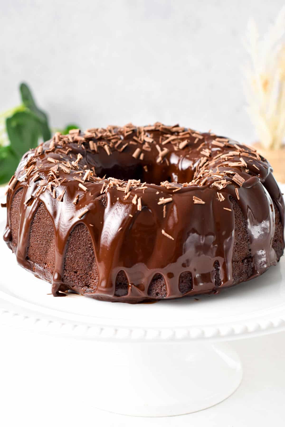 A chocolate Bundt Cake on a cake stand with drippy chocolate ganache and grated chocolate.