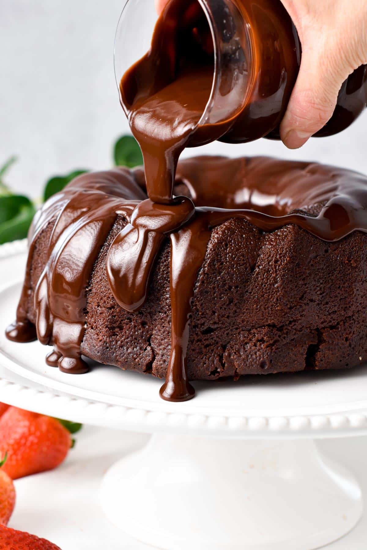 Pouring vegan chocolate ganache on top of a vegan chocolate Bundt cake.