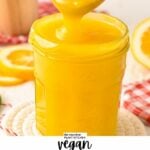 a glass jar filled with vegan lemon curd and a wooden spoon pouring some curd in the jar