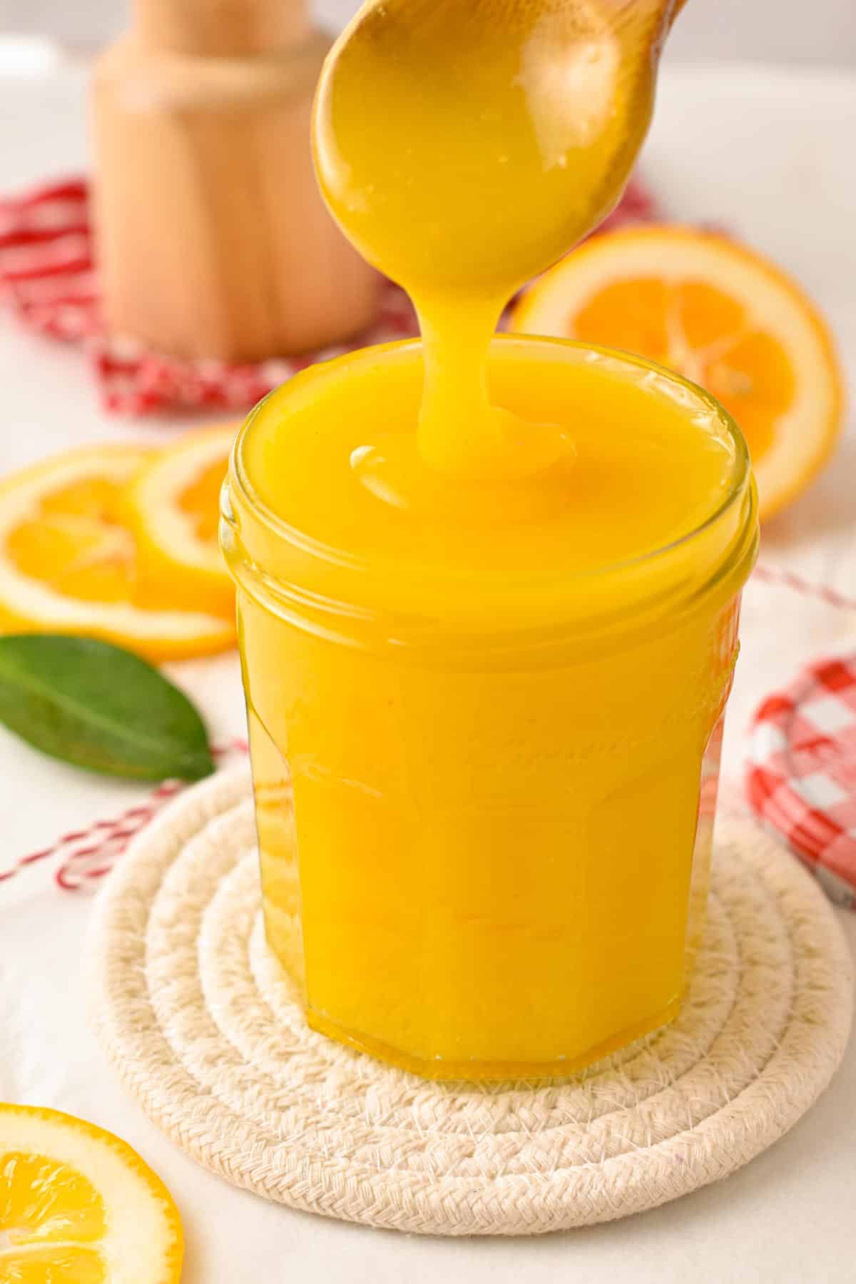 A glass jar filled with vegan lemon curd and a wooden spoon pouring some curd in the jar.