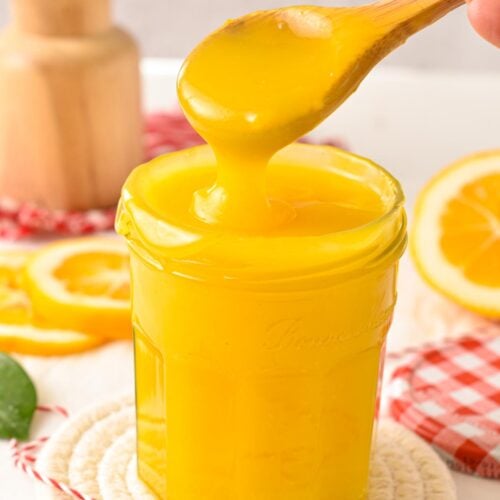 a glass jar filled with vegan lemon curd and a wooden spoon pouring some curd in the jar