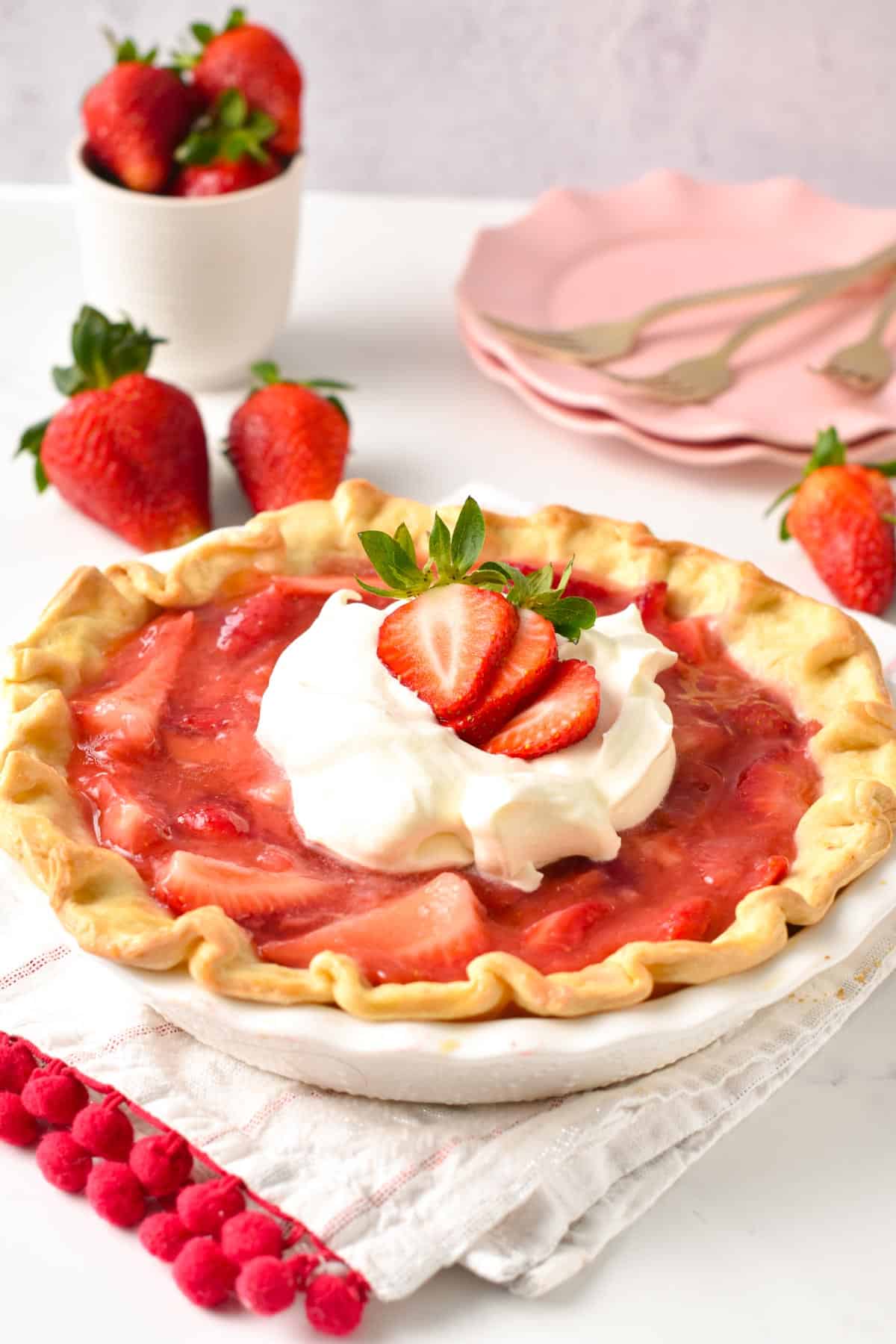 A vegan strawberry pie in a white pie dish topped with dairy-free whipped cream, and fresh strawberry slices.