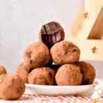 a plate with a pyramid of vegan chocolate truffles coated in cocoa powder, with one truffle on top half bitten showing the fudgy chocolate texture of the truffle