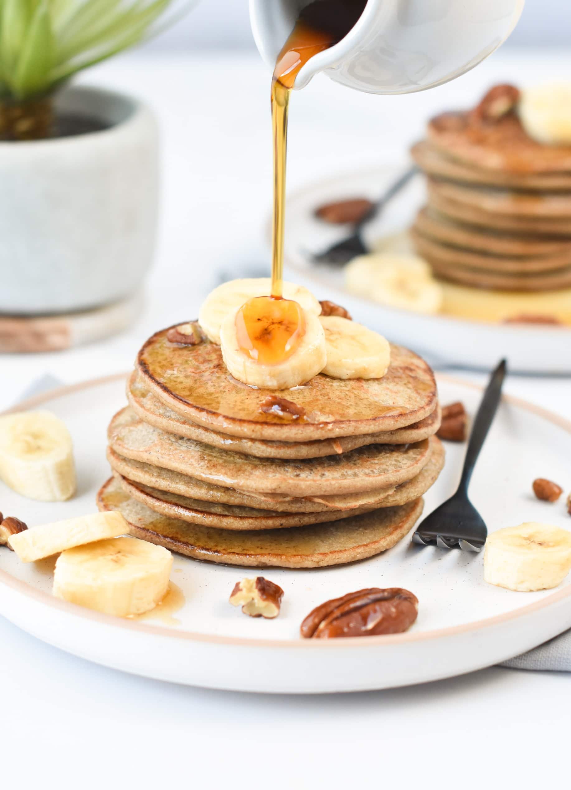 Pouring maple syrup on 3-ingredient banana oat pancakes decorated with banana slices.