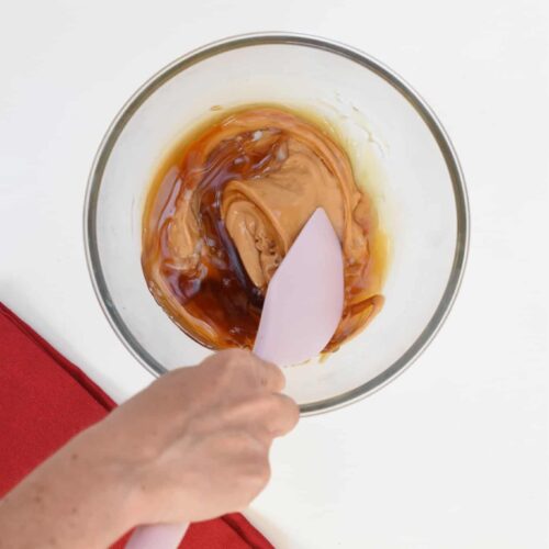 Combining maple syrup and peanut butter in a mixing bowl with a silicone spatula.