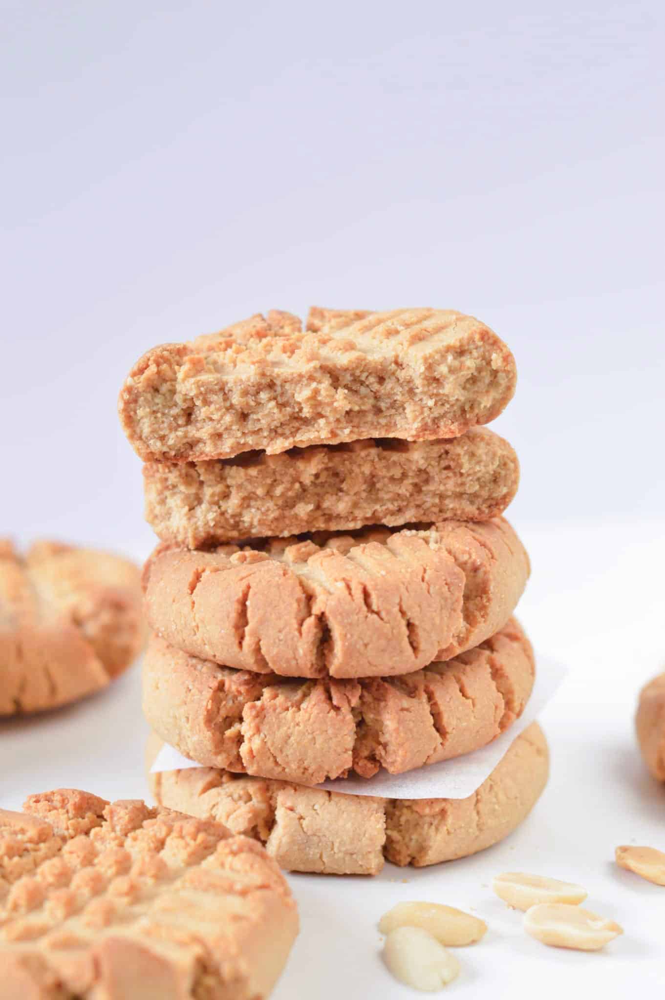 Healthy peanut butter cookies stacked next to fresh peanuts.