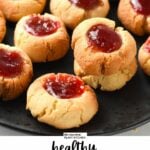 a black plate filled with almond flour thumbprint cookies filled with vibrant red jam