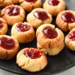 a black plate filled with almond flour thumbprint cookies filled with vibrant red jam
