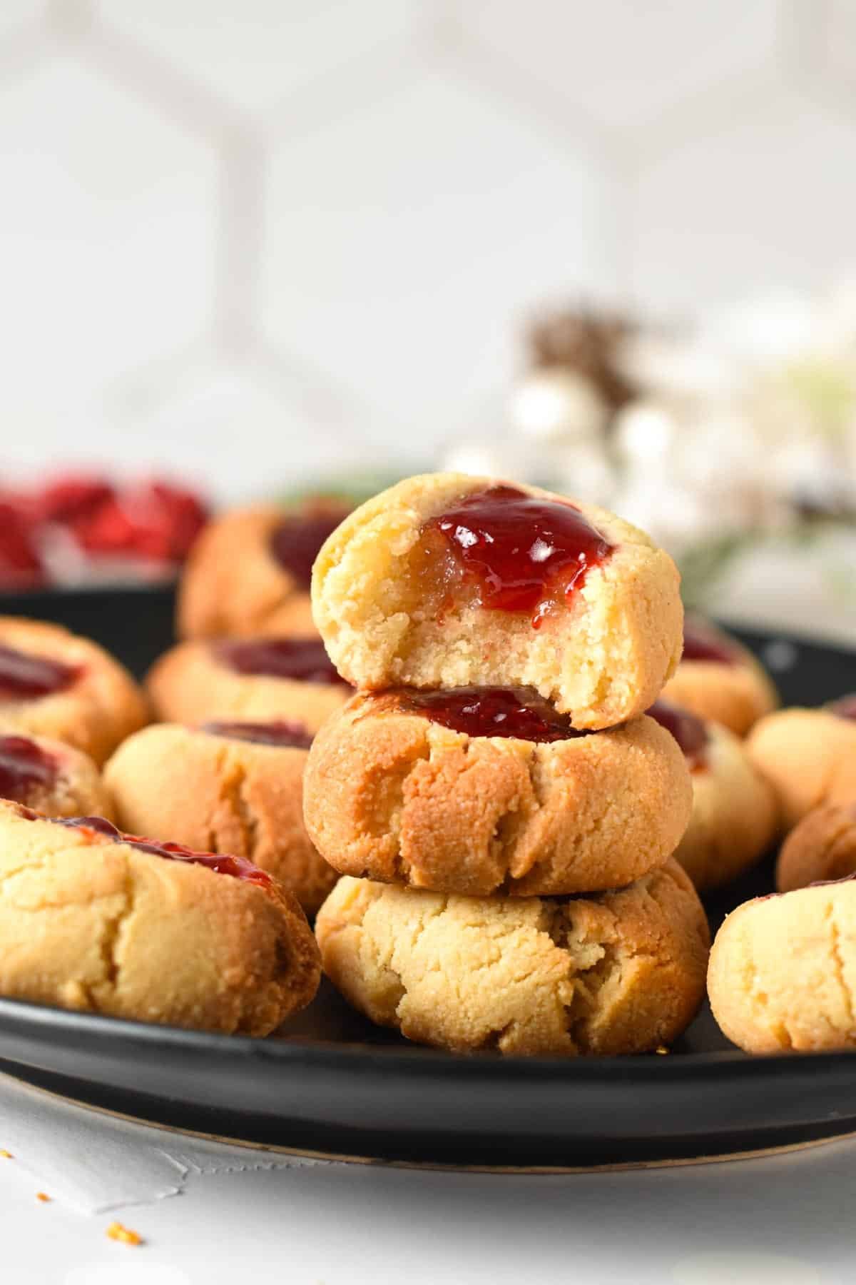 A stack of almond flour thumbprint cookies with the one on top half bitten showing the chewy texture of the cookie.