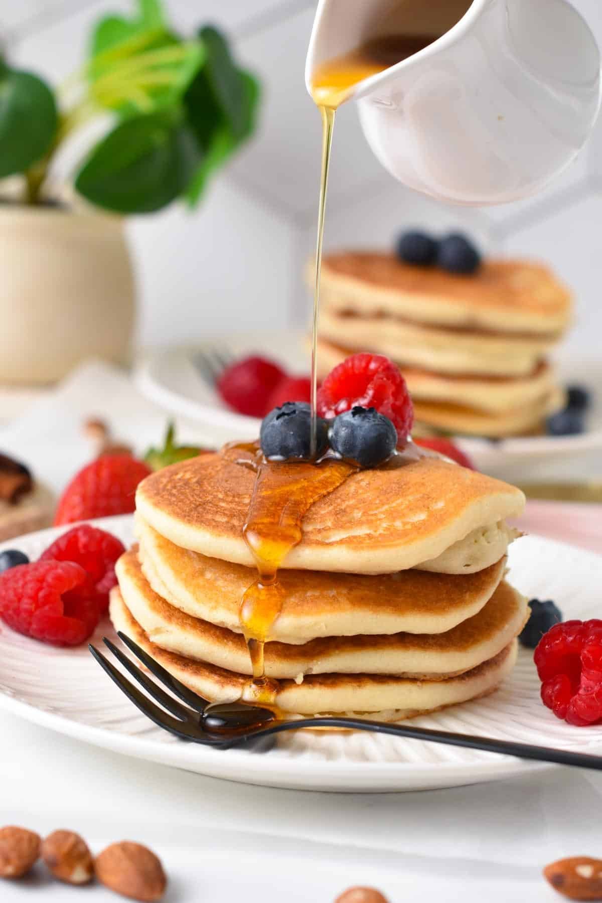 A stack of vegan almond flour pancakes with a drizzle of maple syrup, blueberries and raspberry on top.