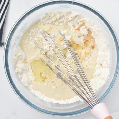 a hand holding a whisk and whisking the wet ingredients into the dry ingredients of a vegan Almond Flour Pancakes batter