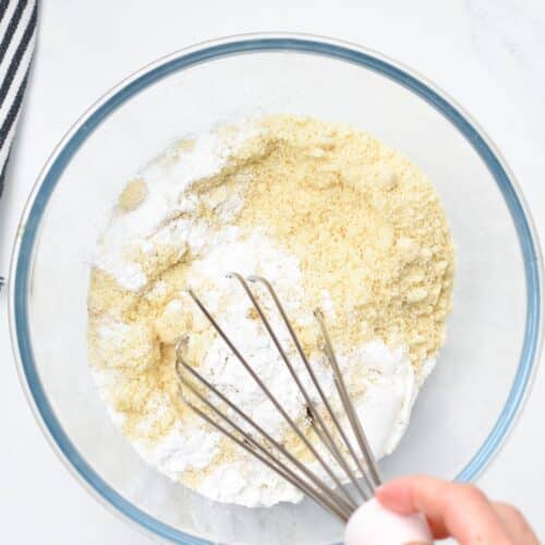 a hand holding a whisk and whisking the dry ingredients of a vegan Almond Flour Pancakes batter