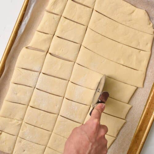 a hand using a pizza cutter to cut a rolled dough into rectangles