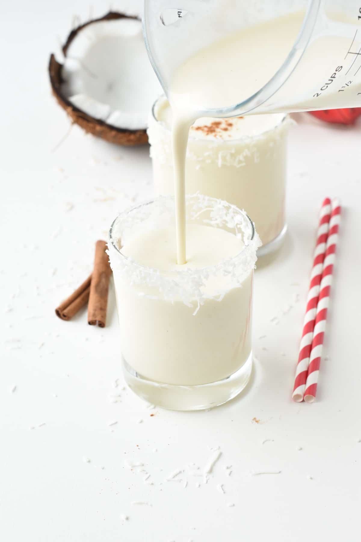 Pouring Vegan Coquito into a glass decorated with coconut