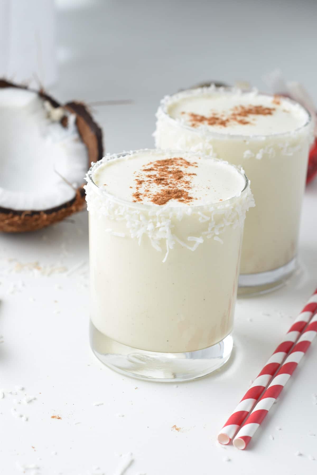 Two glasses of vegan coquito next to an open coconut.