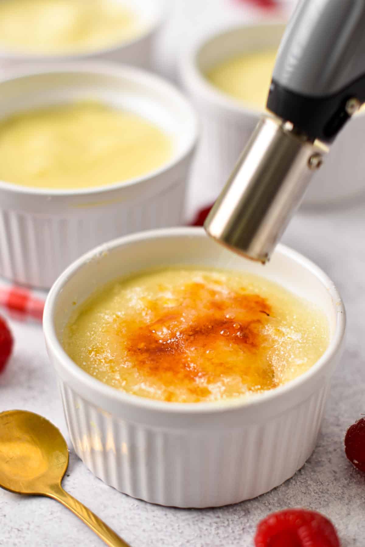 a blow torch burning the top of a creme brulee in a ramekin