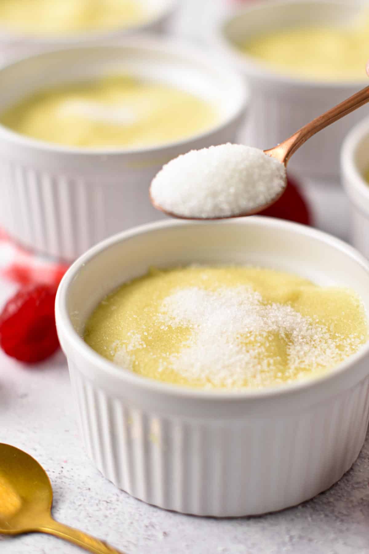 a spoon sprinkling white sugar on top of a creme brulee in a ramekin