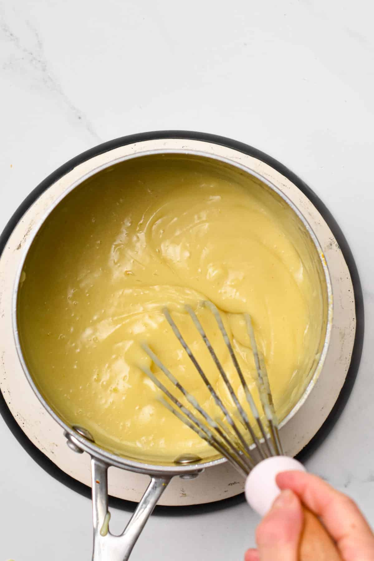 a whisk, whisking a creamy smooth creme brulee mixture in a saucepan