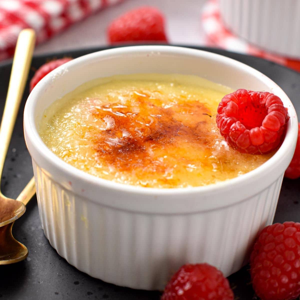 a ramekin filled with a creme brulee mixture topped with crunchy caramel golden layer and a fresh raspberry on side