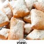 a cooling rack loaded with vegan beignets dusted with powdered sugar and a pot of red jam in the background