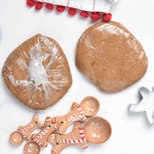 Vegan Gingerbread Cookies dough wrapped in plastic wrap next to themed measuring spoons.