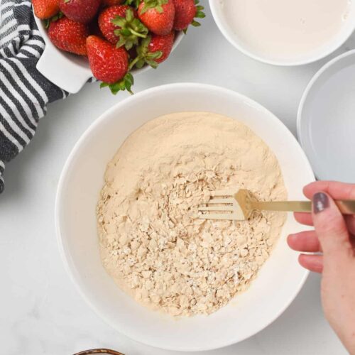 Stirring protein powder and oats in a bowl with a golden spoon.