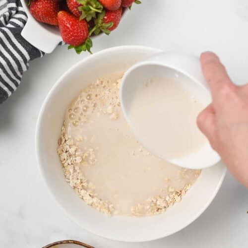 Adding almond milk to the protein powder oatmeal bowl.