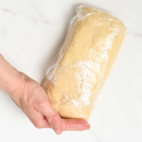 Log of vegan shortbread cookie dough wrapped in plastic wrap.