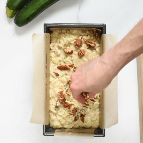 Adding chopped pecans on the Healthy Zucchini Banana bread batter in a loaf pan.
