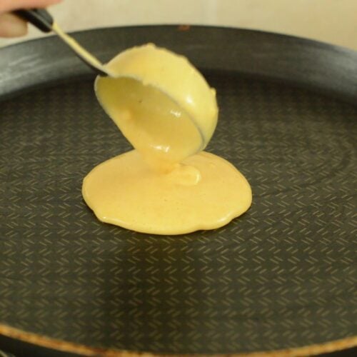 pouring chickpea flour pancake batter on crepe pan