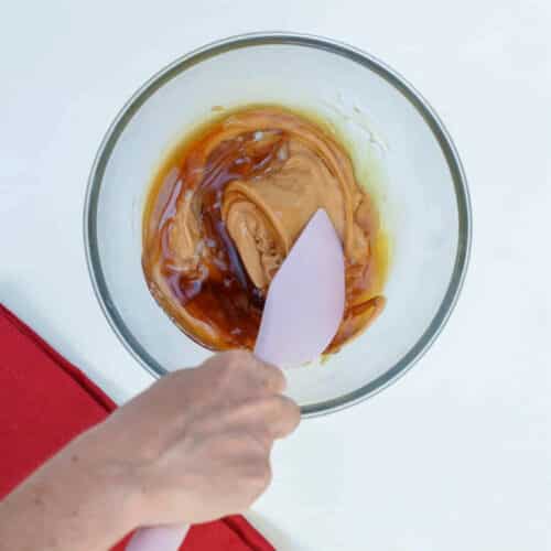 Mixing peanut butter and maple syrup in a mixing bowl.