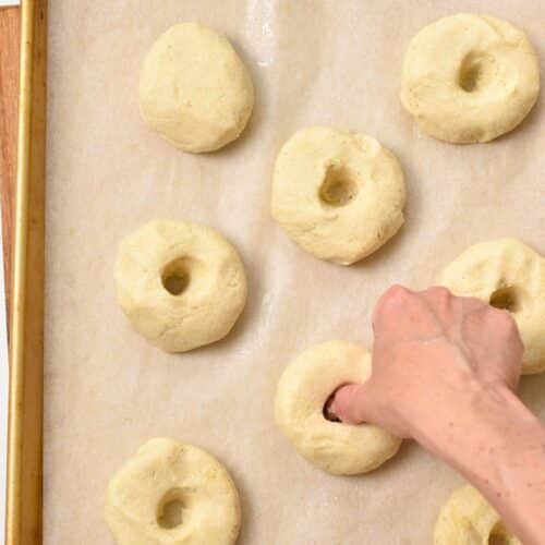 A baking sheet covered with almond flour bagels a thumb forming the hole in the center of one bagel.