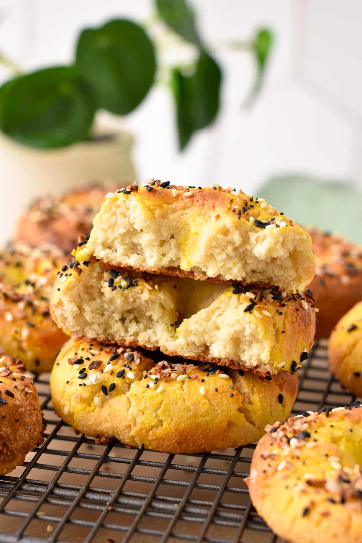 A stack of almond flour bagels on a cooling rack with the top one half broken showing the texture of the bagel.