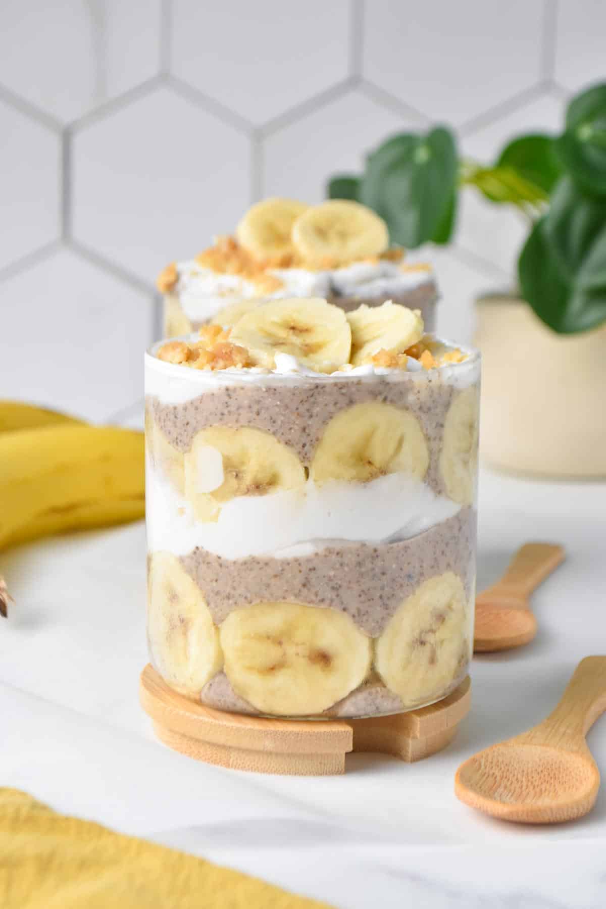 Two glass jar filled with banana chia seed pudding and layers of banana slices and coconut yogurt and banana slices on top.