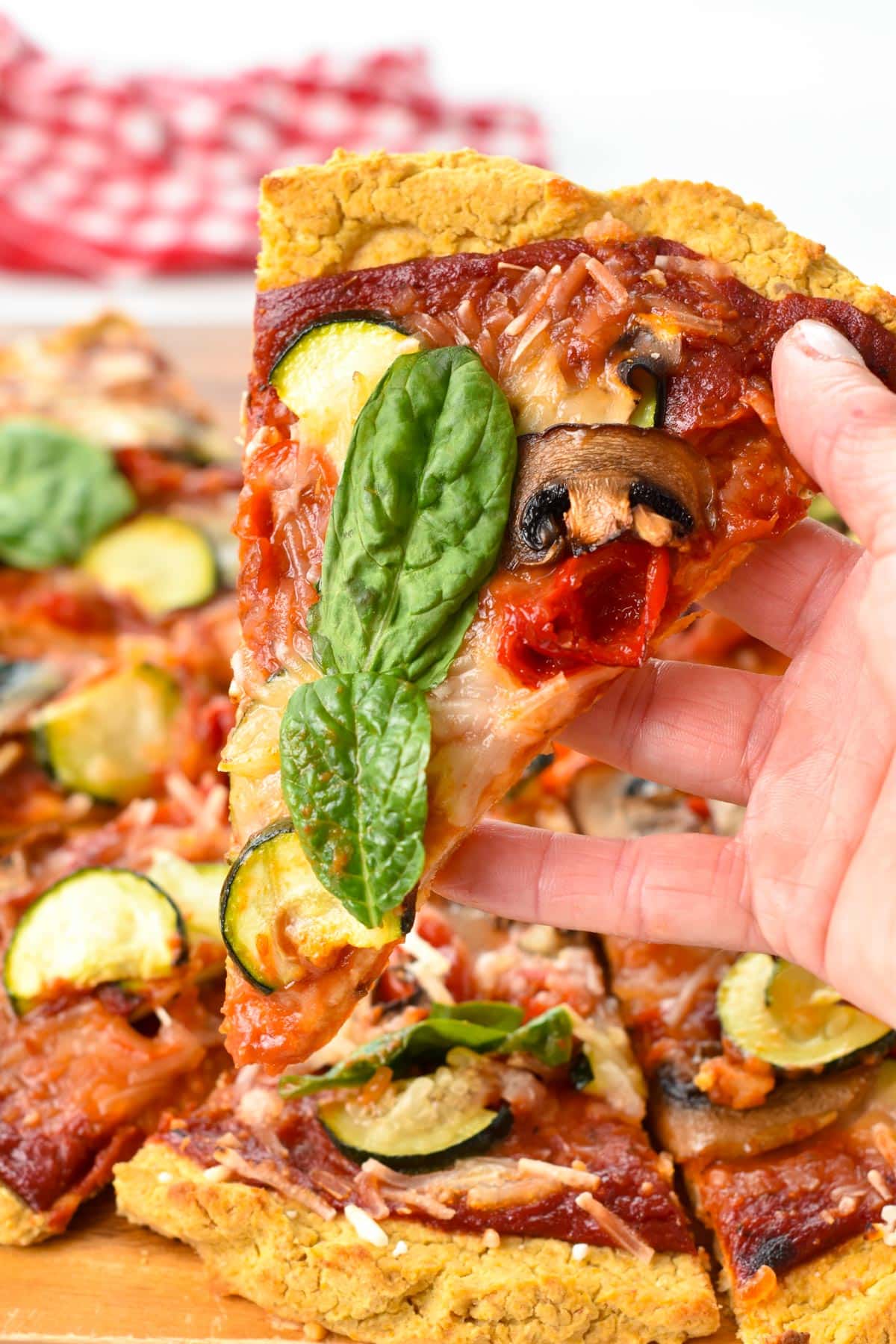 A hand holding a slice of chickpea pizza crust filled with marinara sauce and vegetables.