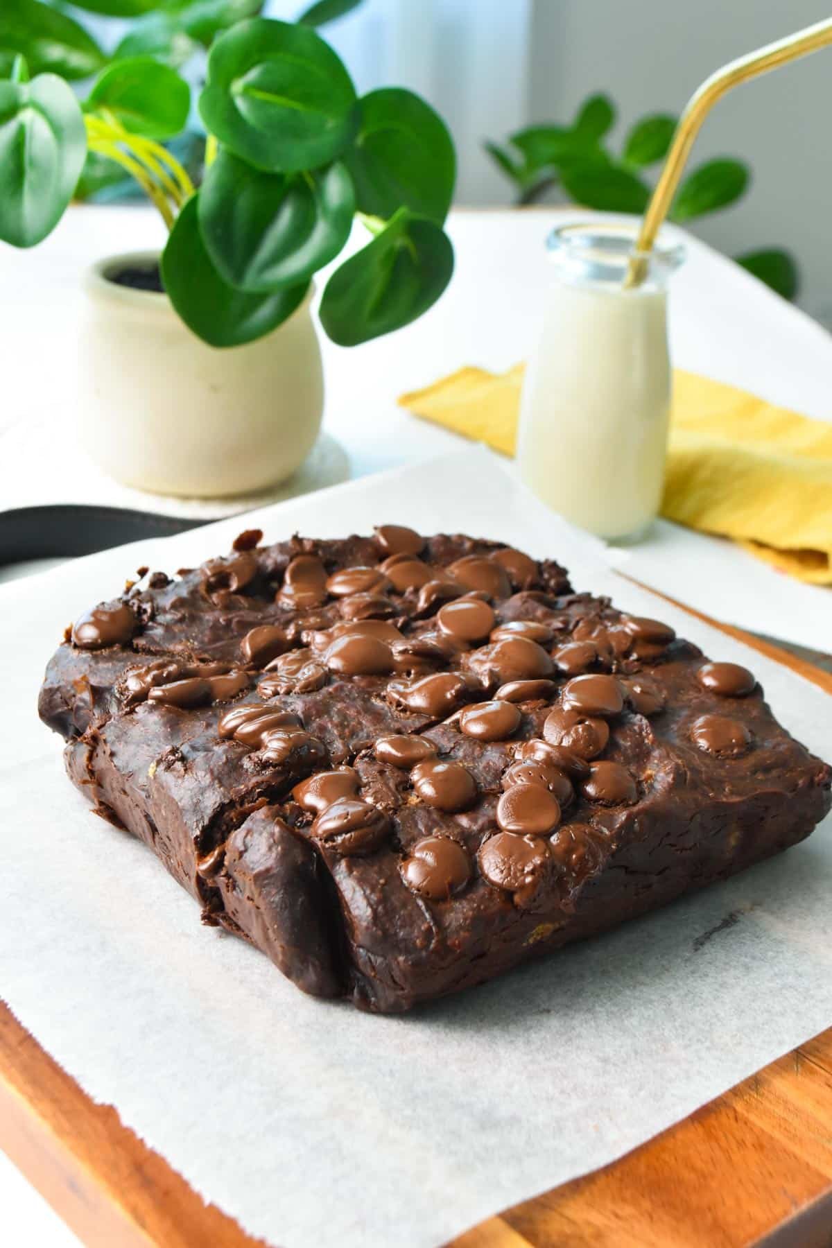 a healthy banana brownies on a wooden board and a green plant in the background with a glass of milk